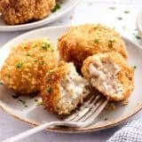 Side view of chicken croquettes on a plate with one sliced in half.
