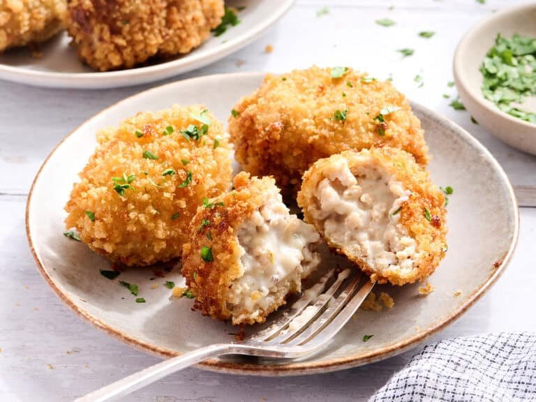 Side view of chicken croquettes on a plate with one sliced in half.