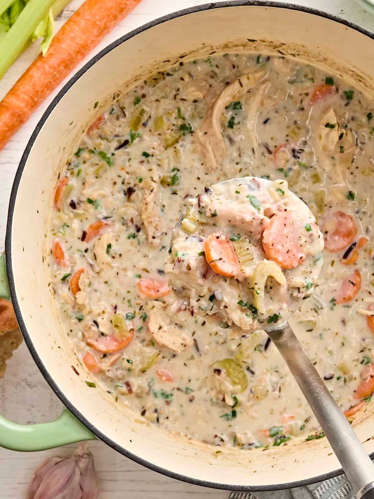 Overhead view of a pot of creamy chicken and rice soup with a ladle taking some.