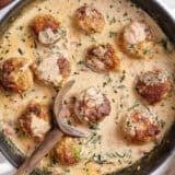Overhead view of marry meatballs in a skillet with a wooden spoon.